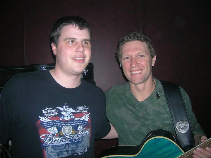 A younger Blind Joe smiling next to a man in a green shirt holding a guitar.